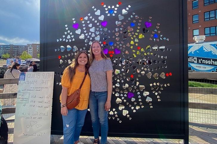 Elizabeth Faraci stands to the right of another person in front of The Mandala Project artwork.